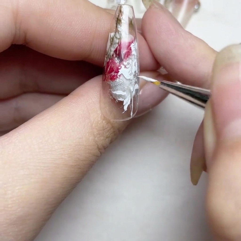 A close-up view of the nail featuring refined white lines and a small, detailed white flower bud being added near the tip.