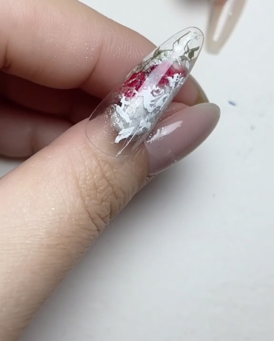 A liner brush applying tiny, clear dabs of gel adhesive onto the surface of a manicured nail.