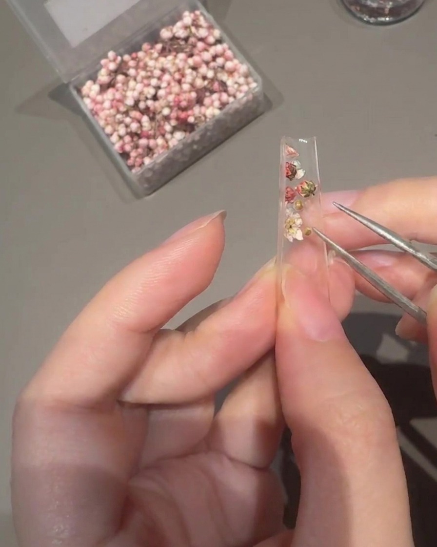 Applying clear extension builder gel over the decorated nail tip with a flat brush.