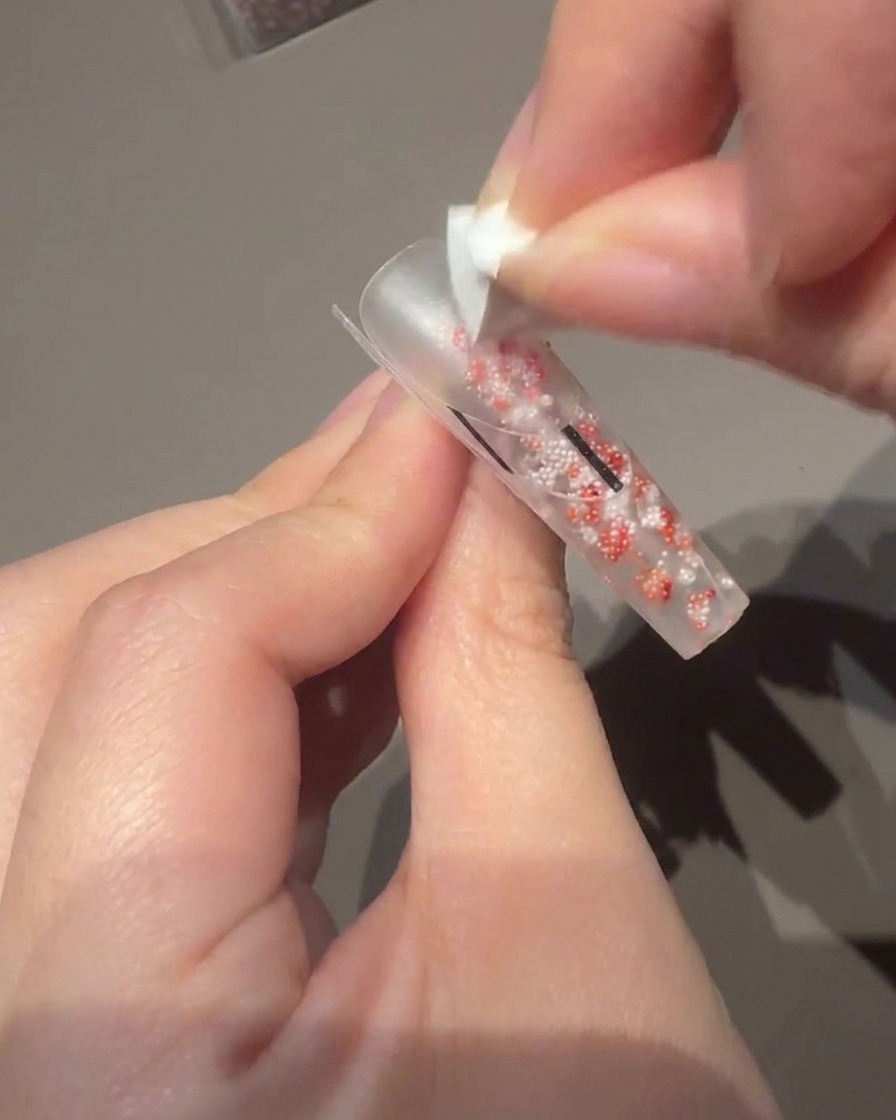 Using a small gel brush to apply a milky pink polish to the nail bed.