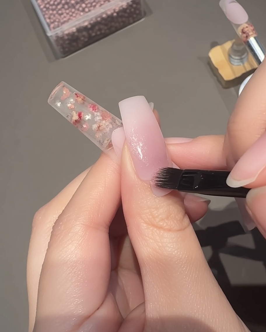 Applying a sheer pink magnetic cat-eye gel over the nail bed with a brush.