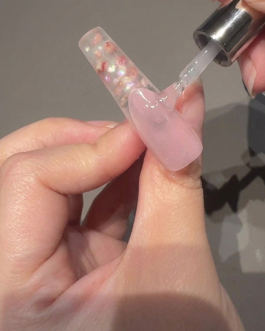 A close-up view of a hand holding a magnetic wand alongside a nail coated in wet cat-eye gel, showing the shimmer moving to the center.