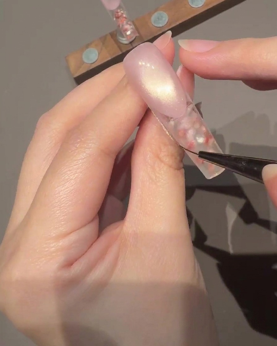 A brush applying a clear, glossy top coat onto the surface of the decorated nail.