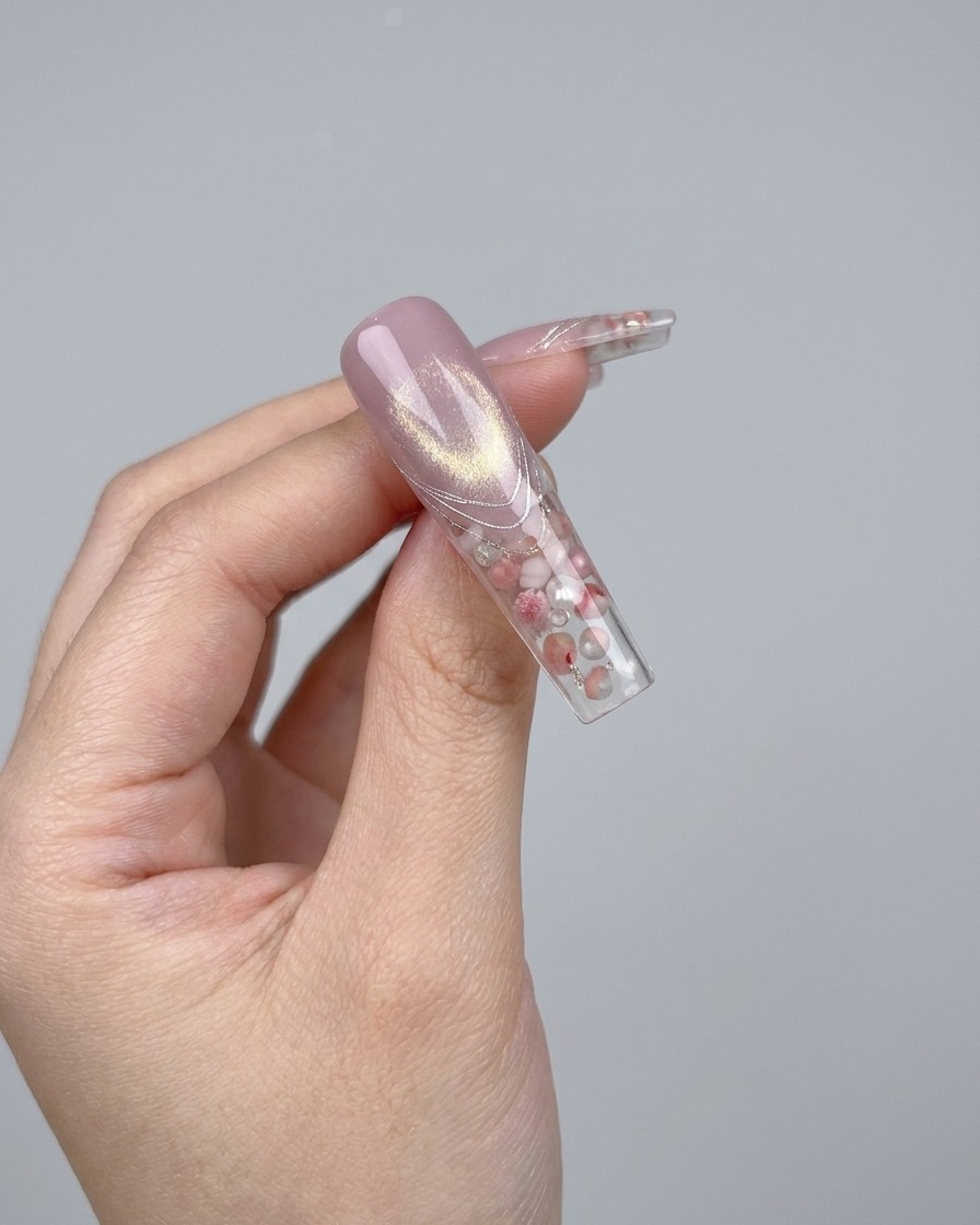 A pair of tweezers placing a small, sparkling 3D crystal bow charm onto a nail.