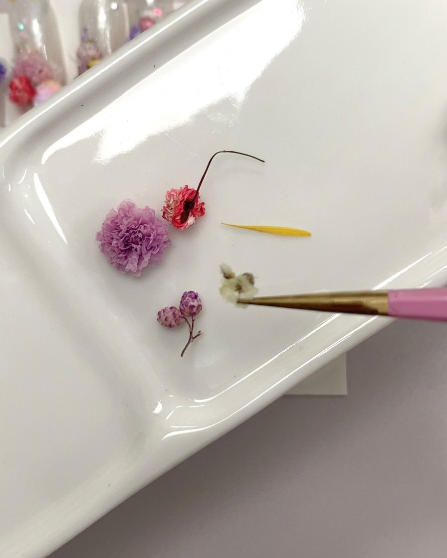 A close-up view of a pair of tweezers holding a dried rose while trimming the stem base.