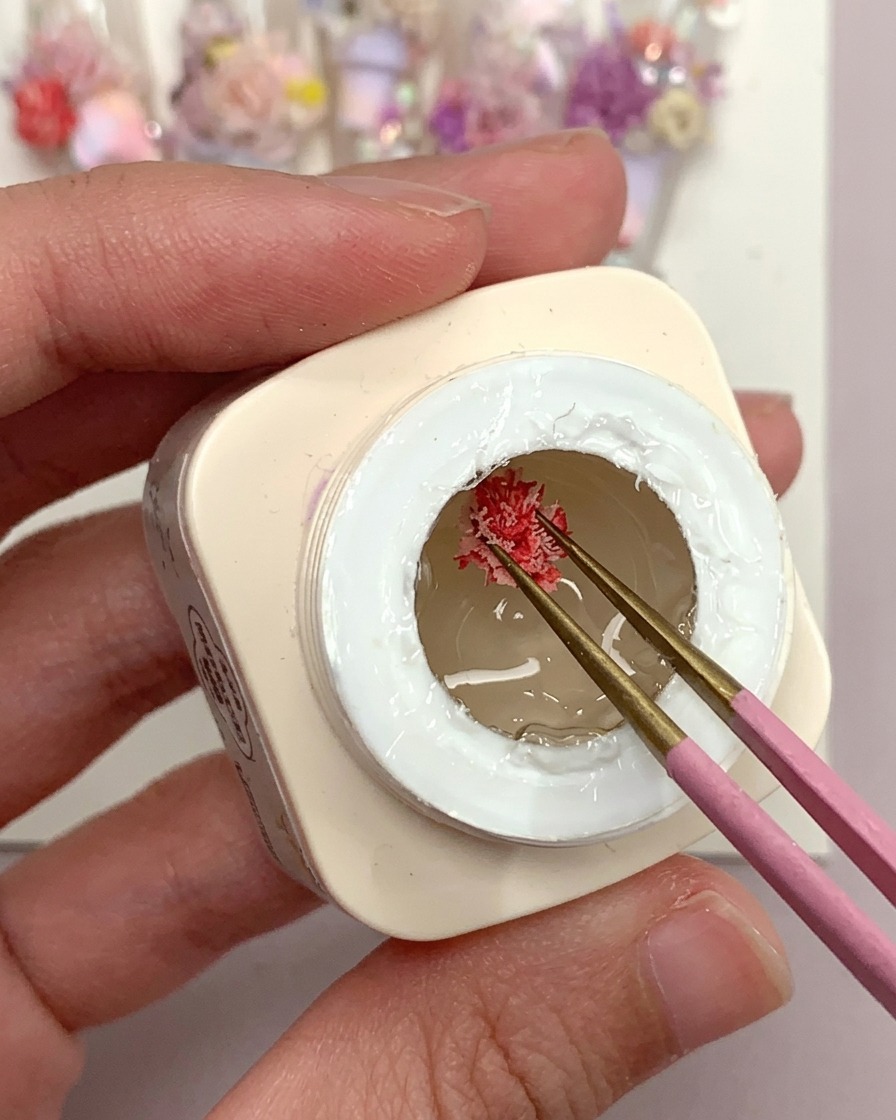 A brush applying a drop of clear frosted gel glue onto a clear plastic nail tip.