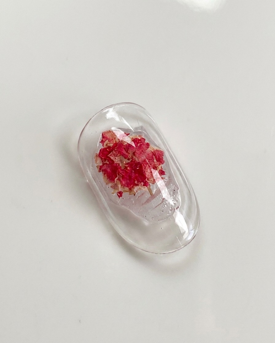 A detail brush gently pressing down on the petals of a dried rose embedded in nail gel.
