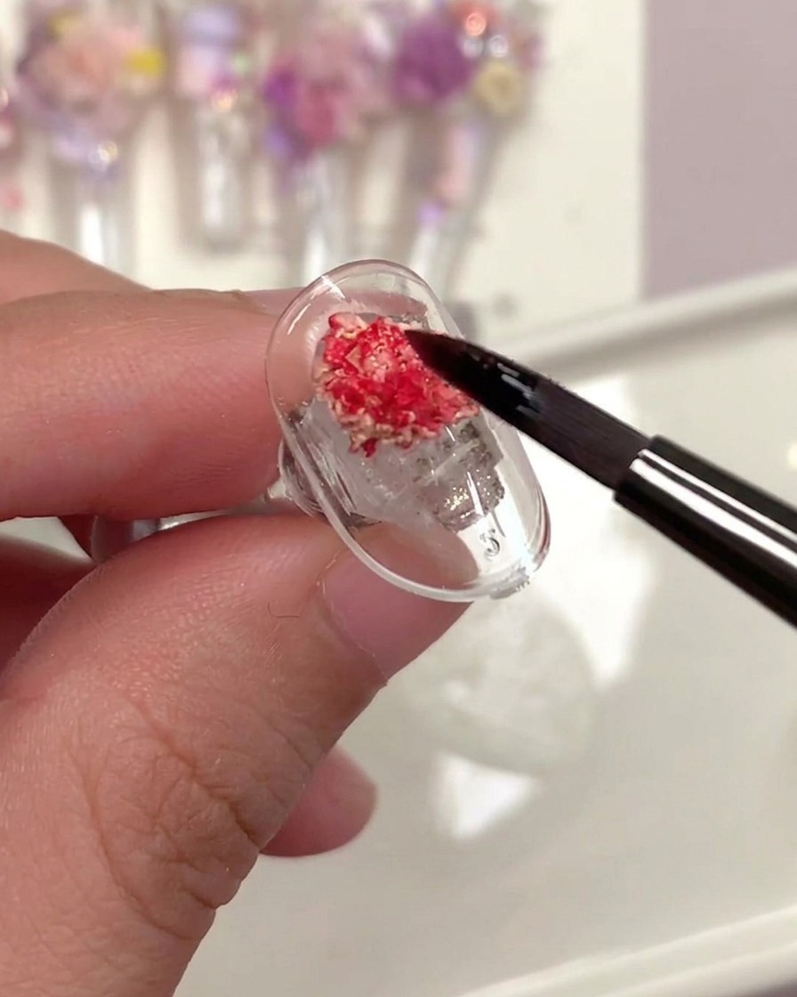 A brush applying a clear top coat over a dried rose on a nail.