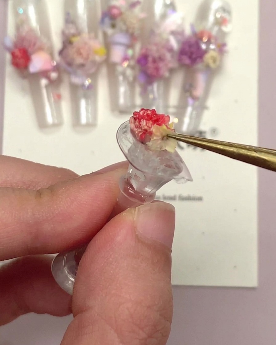 A pair of tweezers holding a small floral nail ornament after it has been encapsulated.