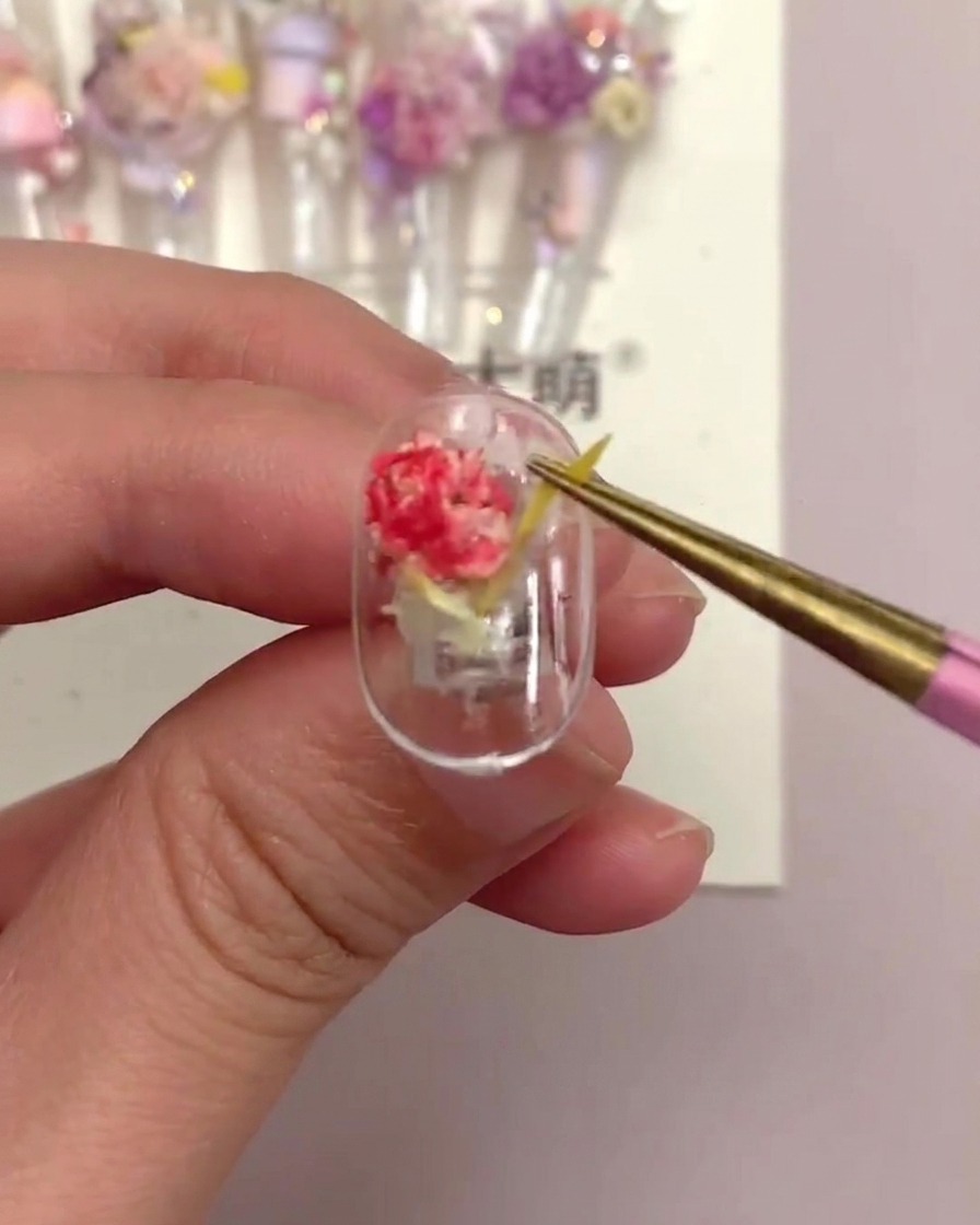 A pair of tweezers gently pulling on a yellow linear flower piece on a finished nail tip to test its security.