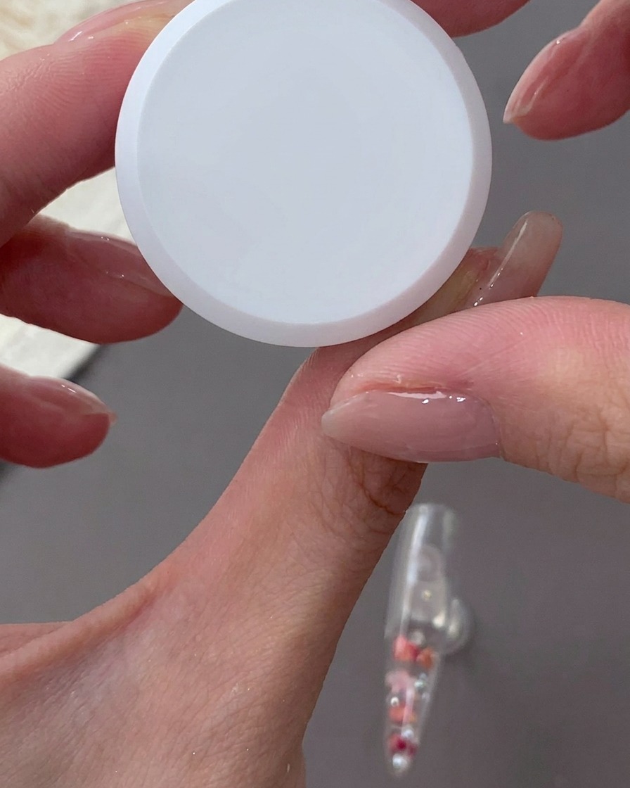 A hand holding a sponge and dabbing milky white gel onto the back edge of a clear nail tip.