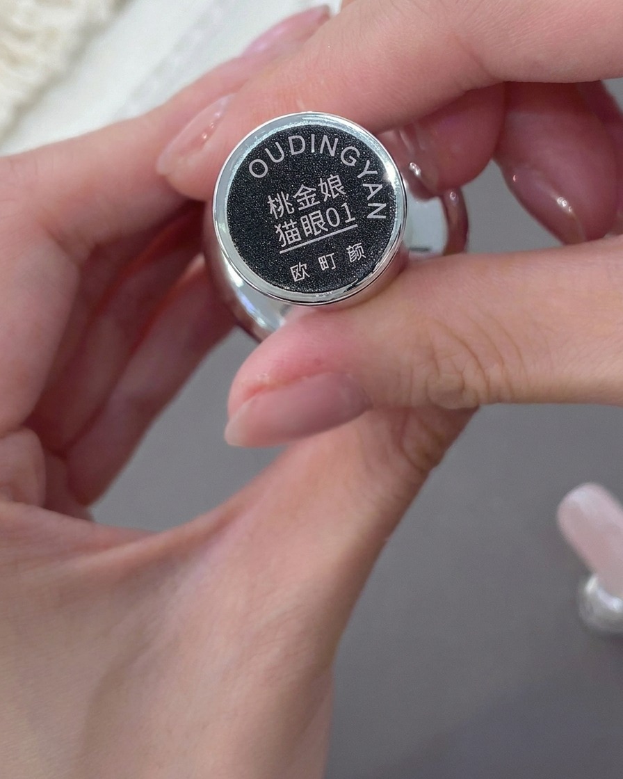 A hand holding a bottle of pinkish-nude cat-eye gel polish, showing the label.