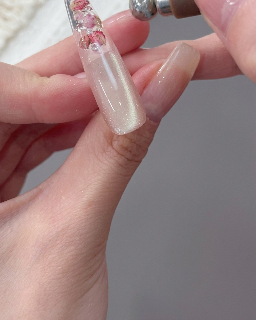 A close-up of a magnet being used to pull magnetic particles into a shimmery band on a nail tip.