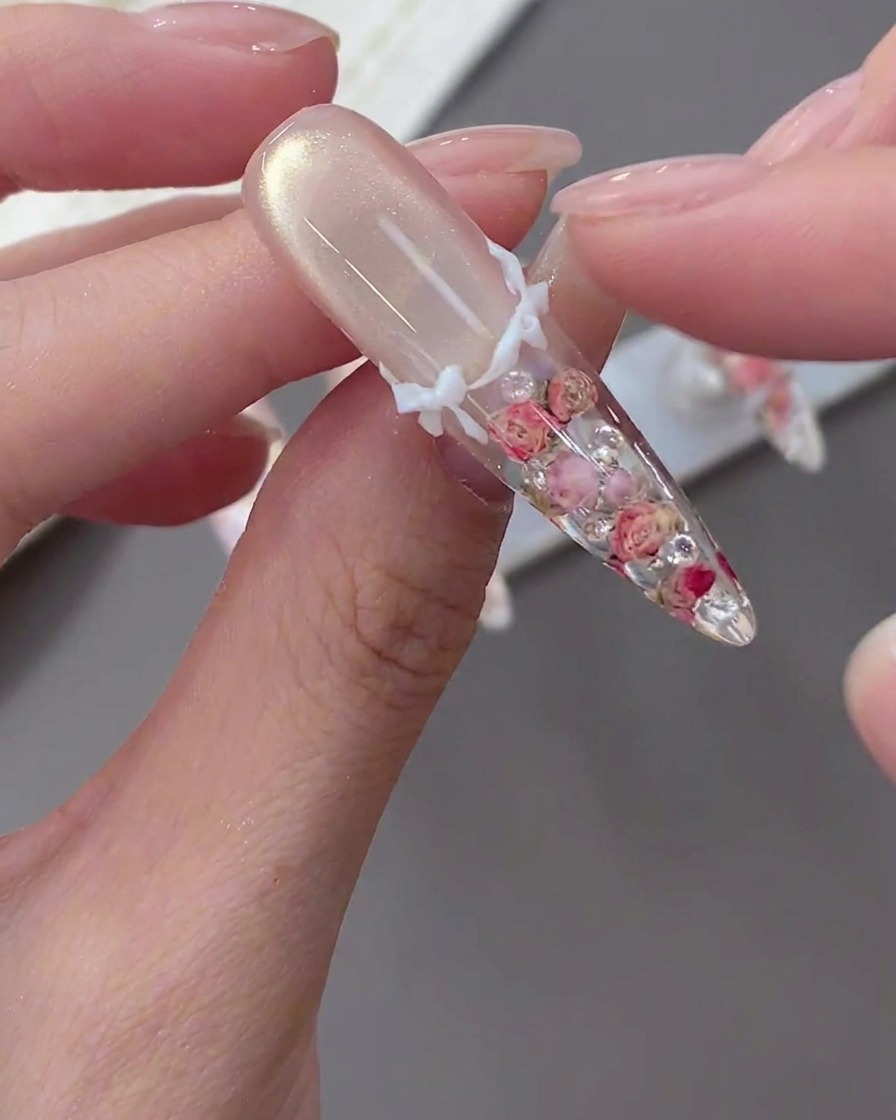 A close-up of a finger placing a white 3D bow onto a decorated nail tip.