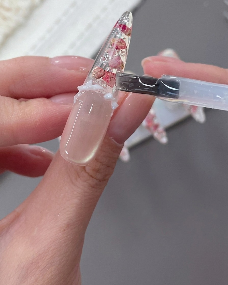 A decorated nail with a white bow, pearls, and rhinestones being finalized.