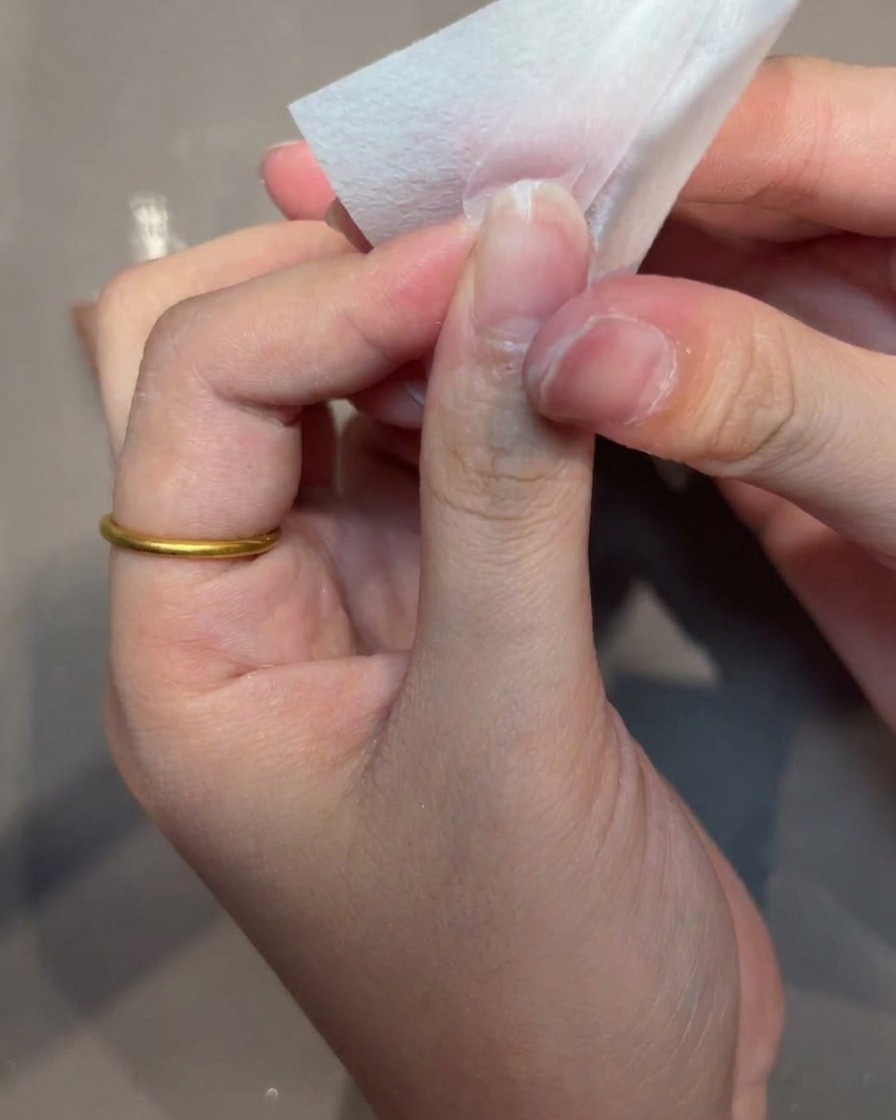 A close-up shot of a hand using a lint-free wipe to clean the surface of a nail tip.