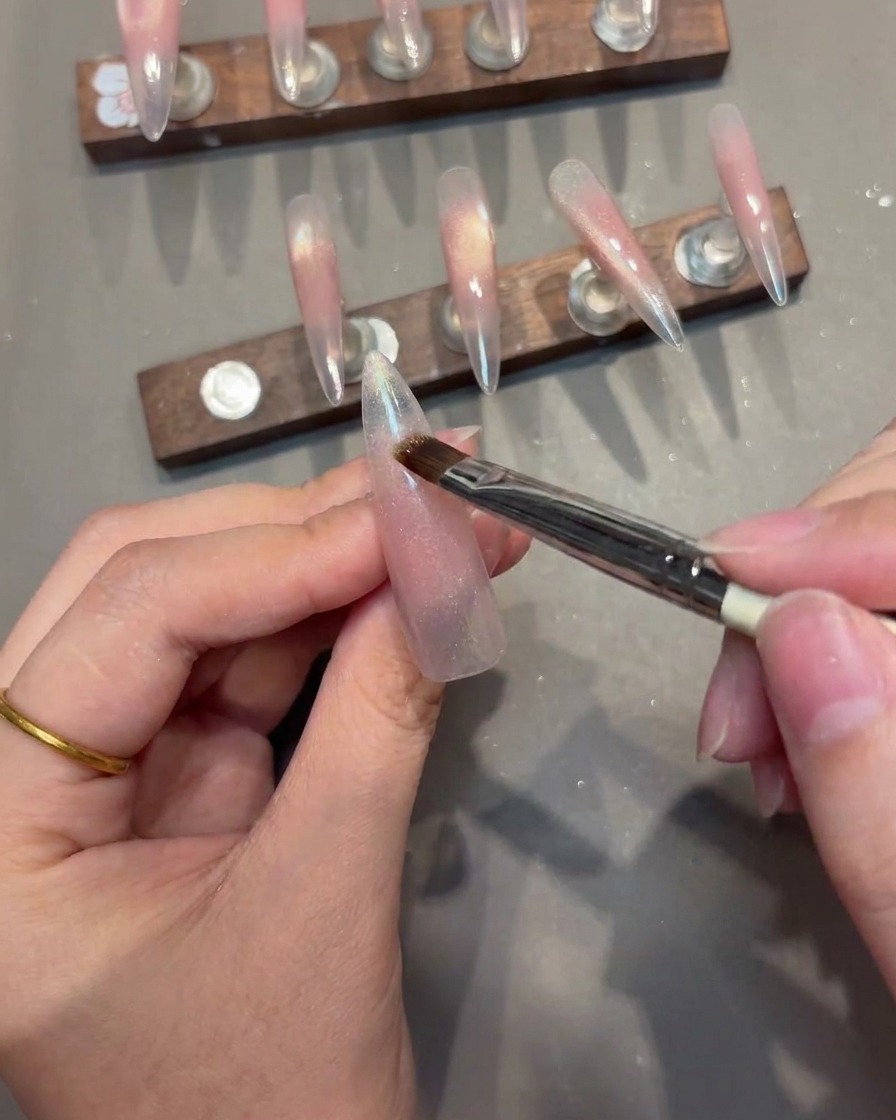A close-up of a nail brush applying magnetic cat-eye gel to a nail tip, with the magnet positioned to create a sharp V-line.