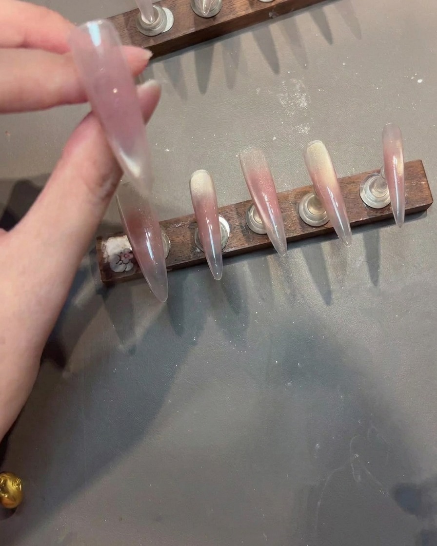 A stamping tool pressing an intricate, irregular white lace design onto a pink cat-eye gel nail.