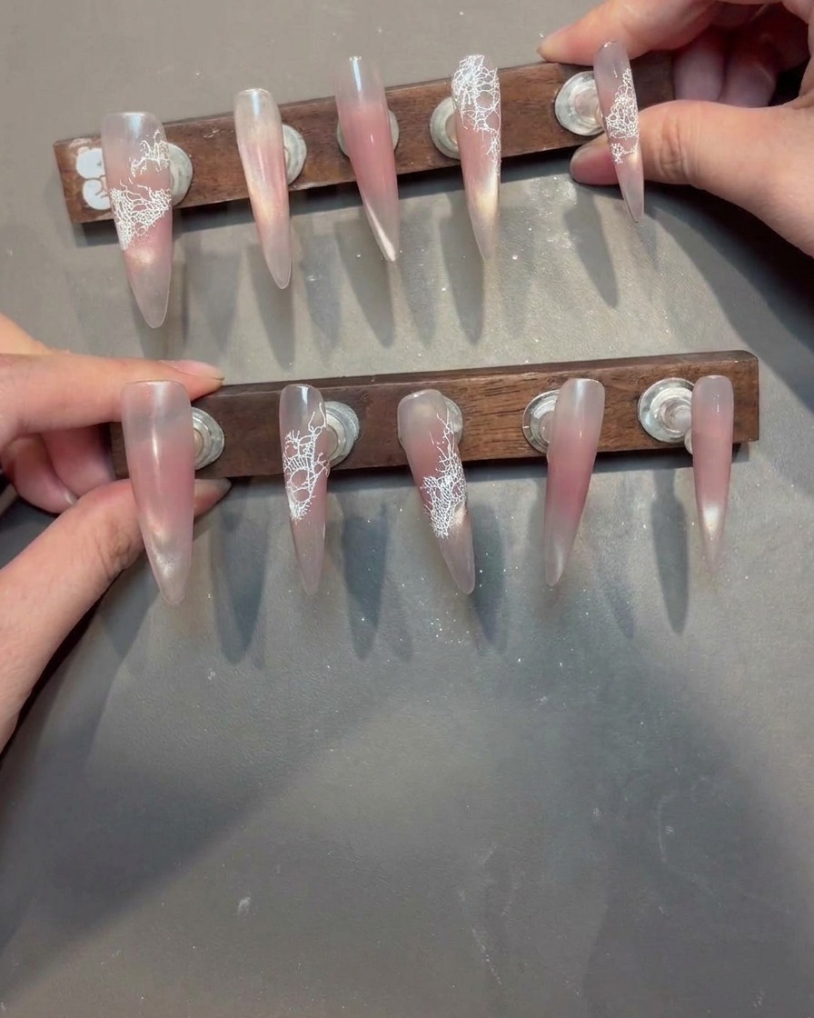 A brush applying a clear, viscous reinforcement gel over a nail with a white lace pattern.