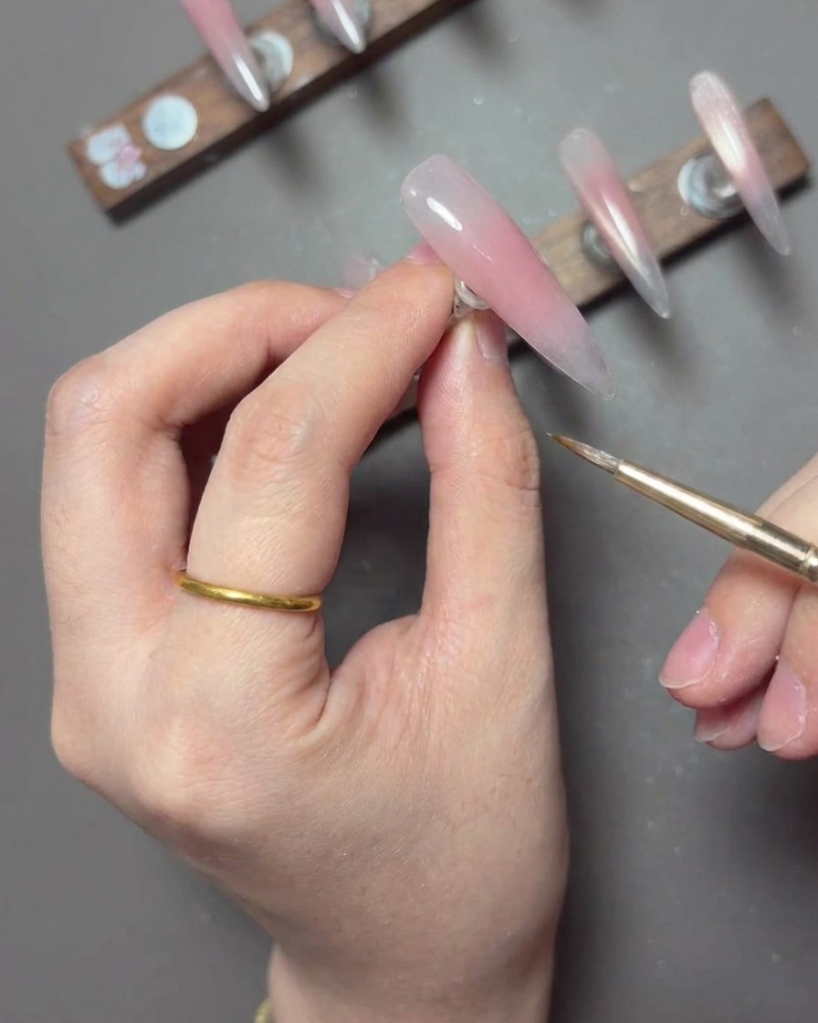 A fine liner brush pulling a thin, stretchy line of white spider gel across a manicured nail to create lace-like details.