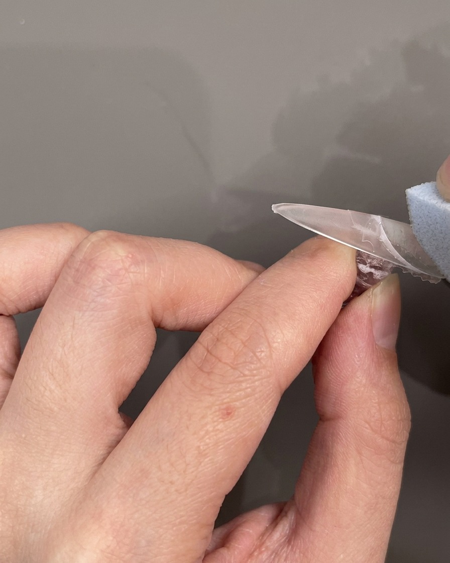 A silicone French smile line sticker placed horizontally across a nail to mask the area for the tip application.