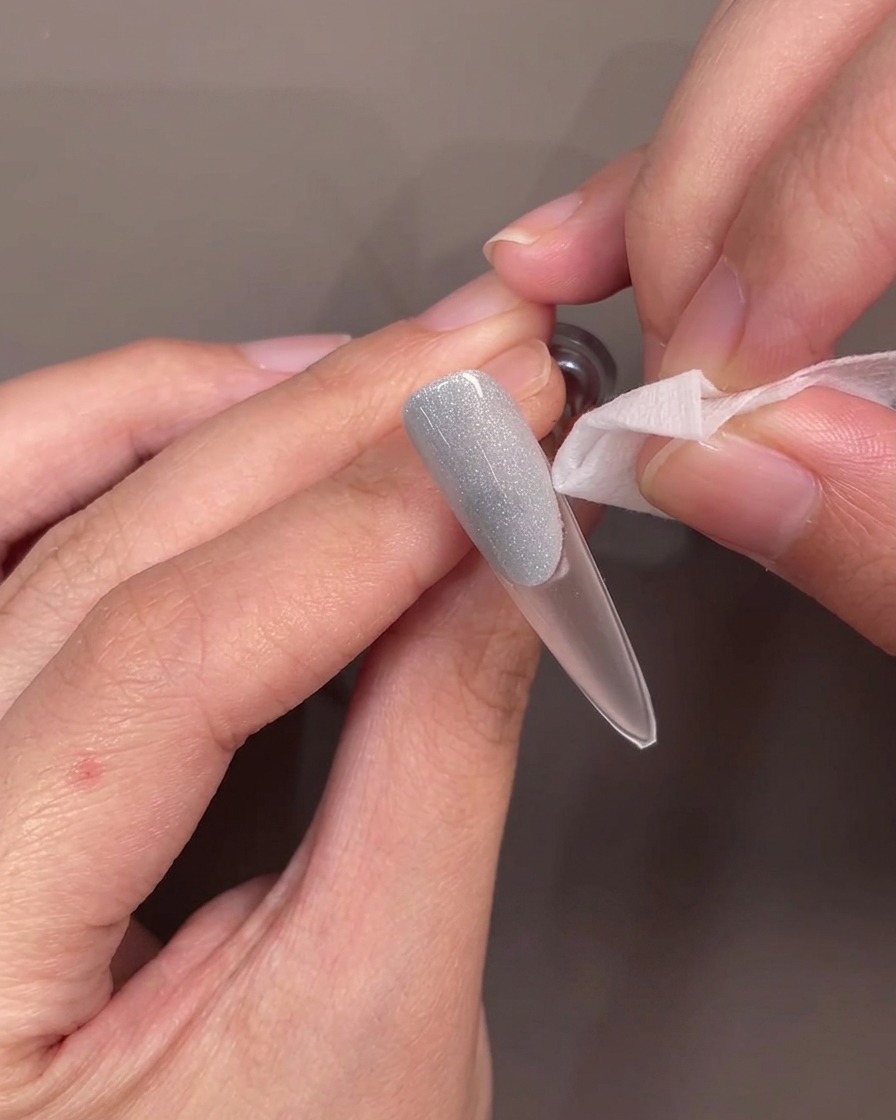 Tweezers lifting a silicone smile line guide off a nail, revealing a clean, curved edge on the blue gel.