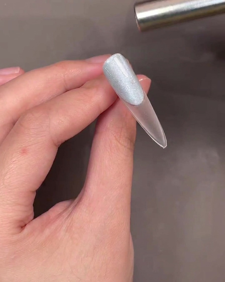 A magnetic wand being held over a blue cat-eye gel-coated nail to create a shimmer effect.