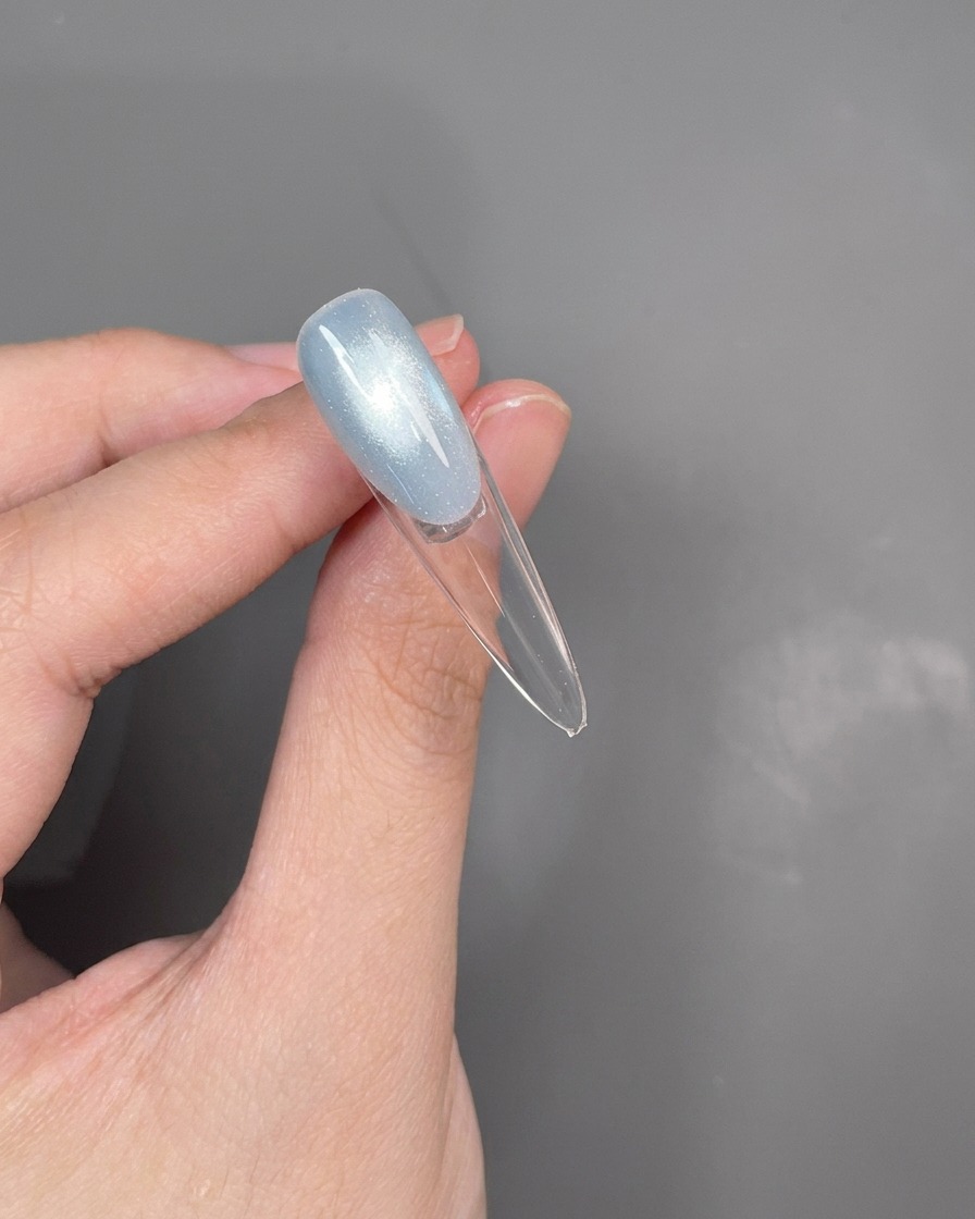 A close-up view of a dotting tool creating a thin silver line along the smile line of a French manicure.