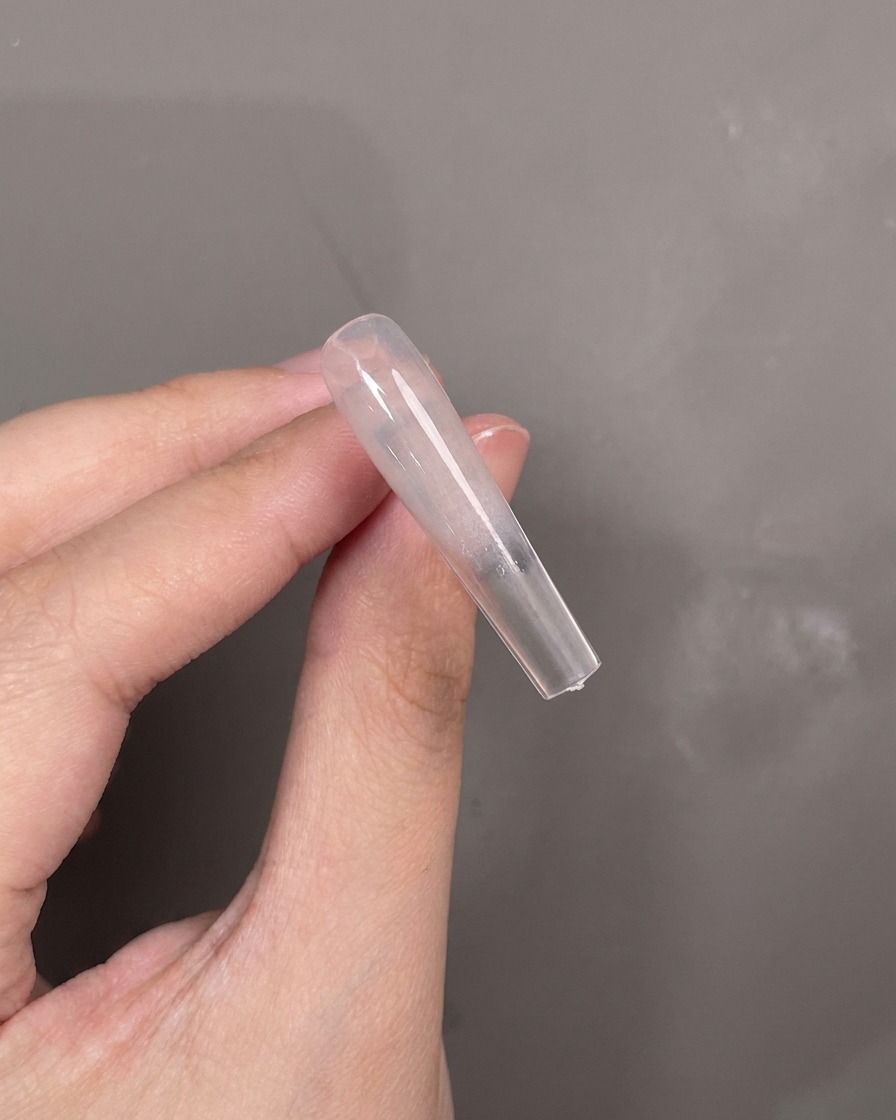 A blue silicone tool applying white texture gel horizontally across the center of a nail tip.