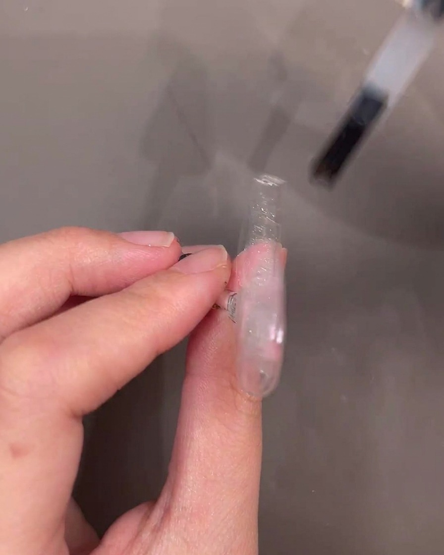 A gel polish bottle brush applying a layer of clear reinforcement gel over a decorated nail tip.