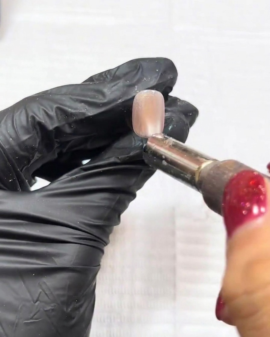 A close-up shot showing a magnet being used over a nail to manipulate the cat-eye particles into a defined central bead.