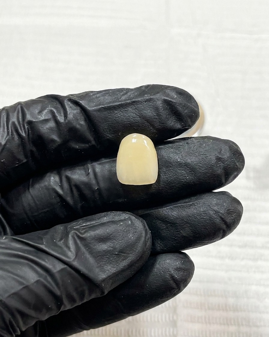 A close-up view of a single nail with cured dark line art being placed under a small UV lamp for curing.
