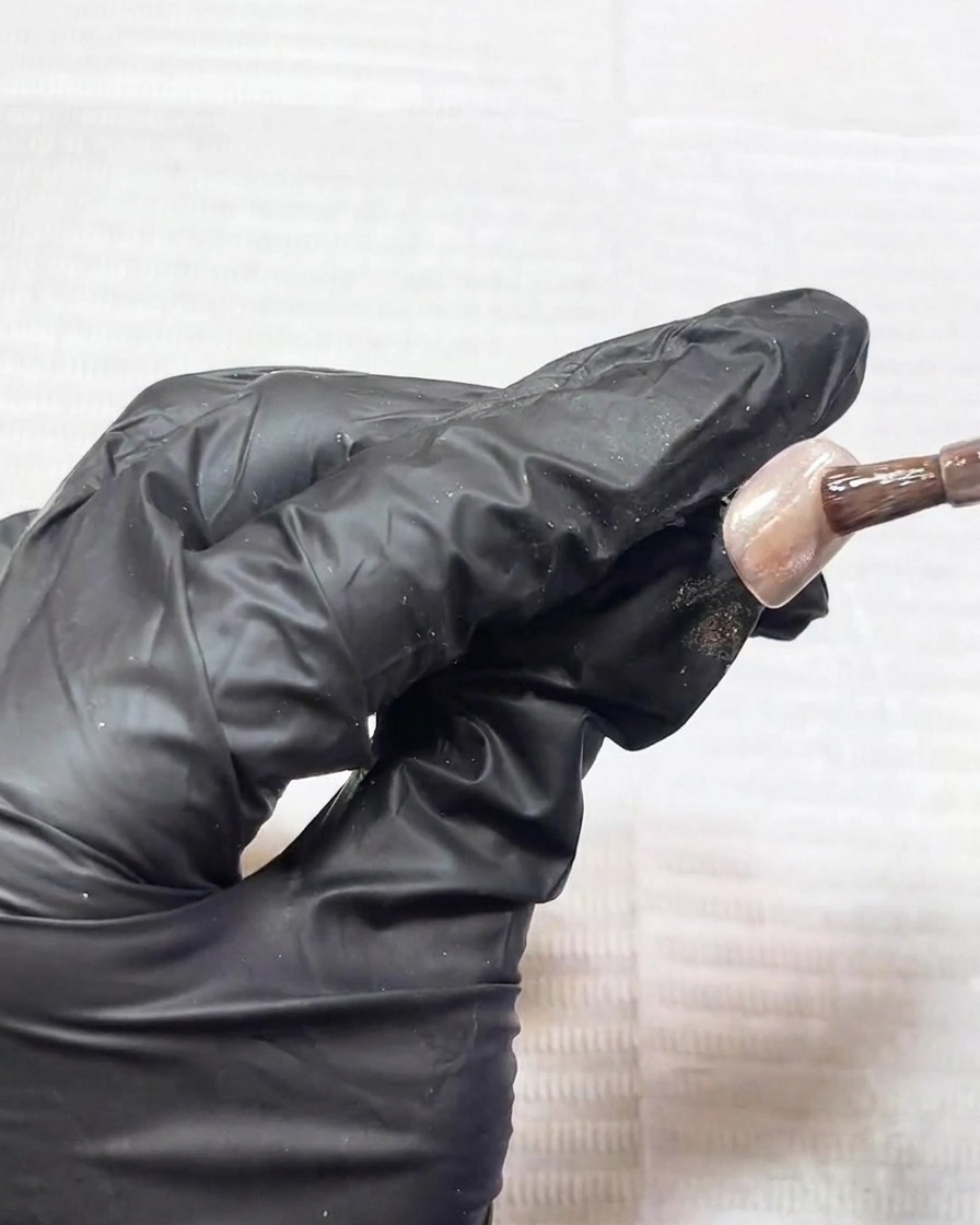 A close-up of a magnetic nail tool being held over a nail coated in cat-eye gel, showing the shifting metallic particles.