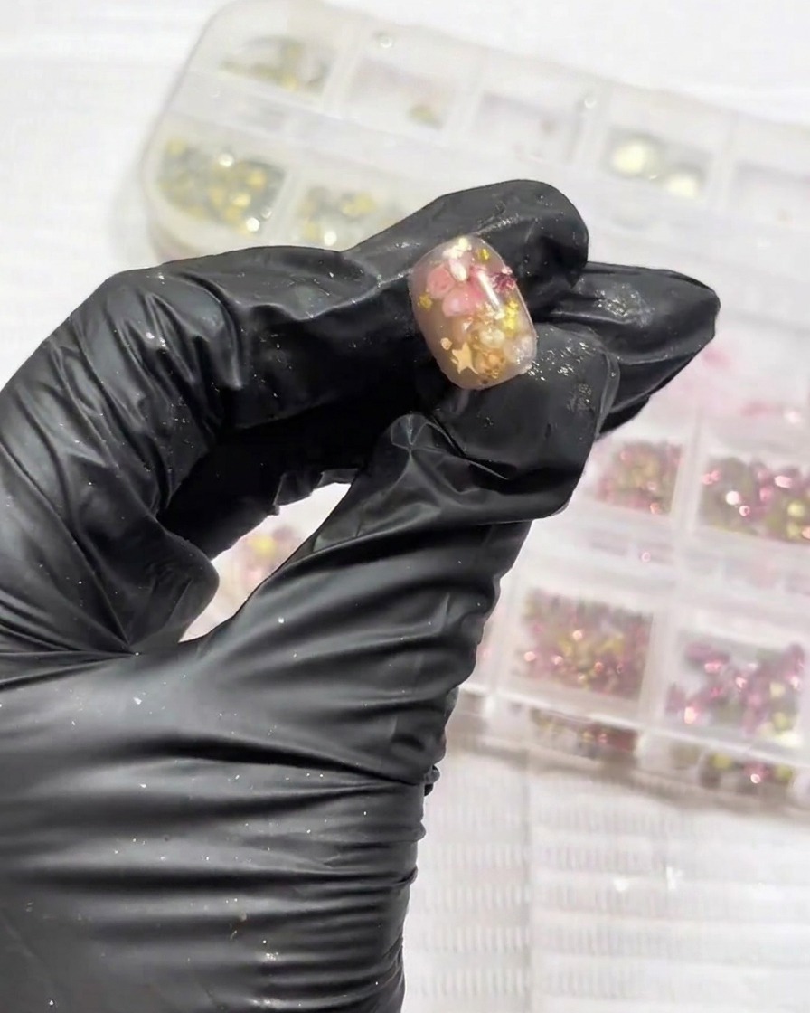 A close-up view of small, sparkling rhinestones being placed into the corner of a decorated nail.