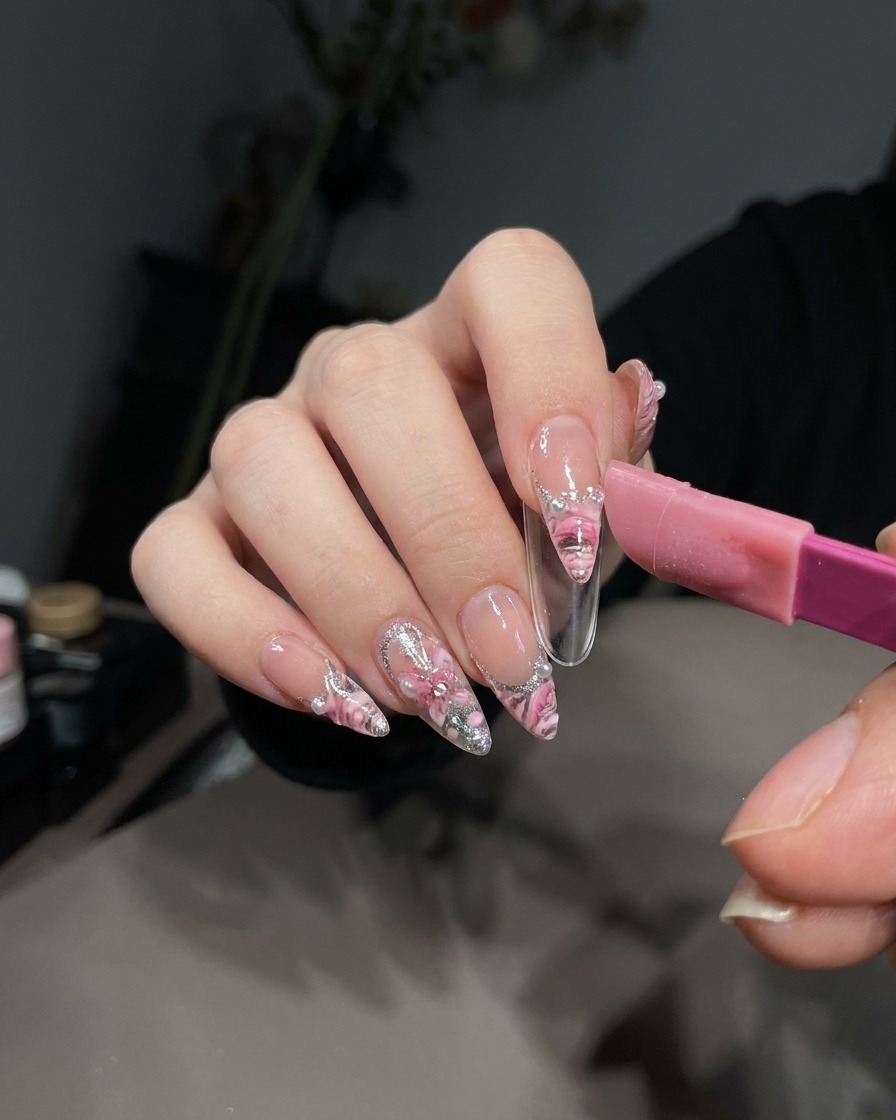 A pair of tweezers carefully lifting a French sticker off the cured white gel on a nail tip.