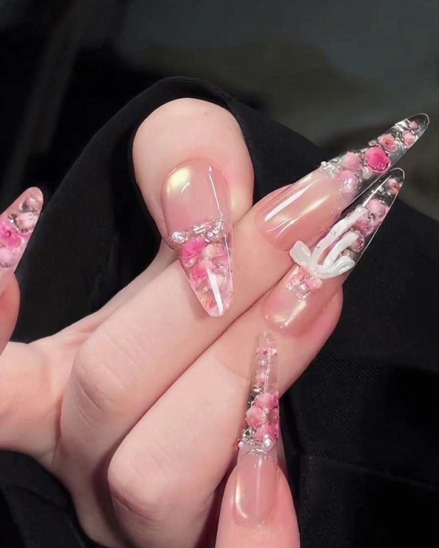 A precision brush placing tiny white pearls and rhinestones onto the floral design on the back of the nail.
