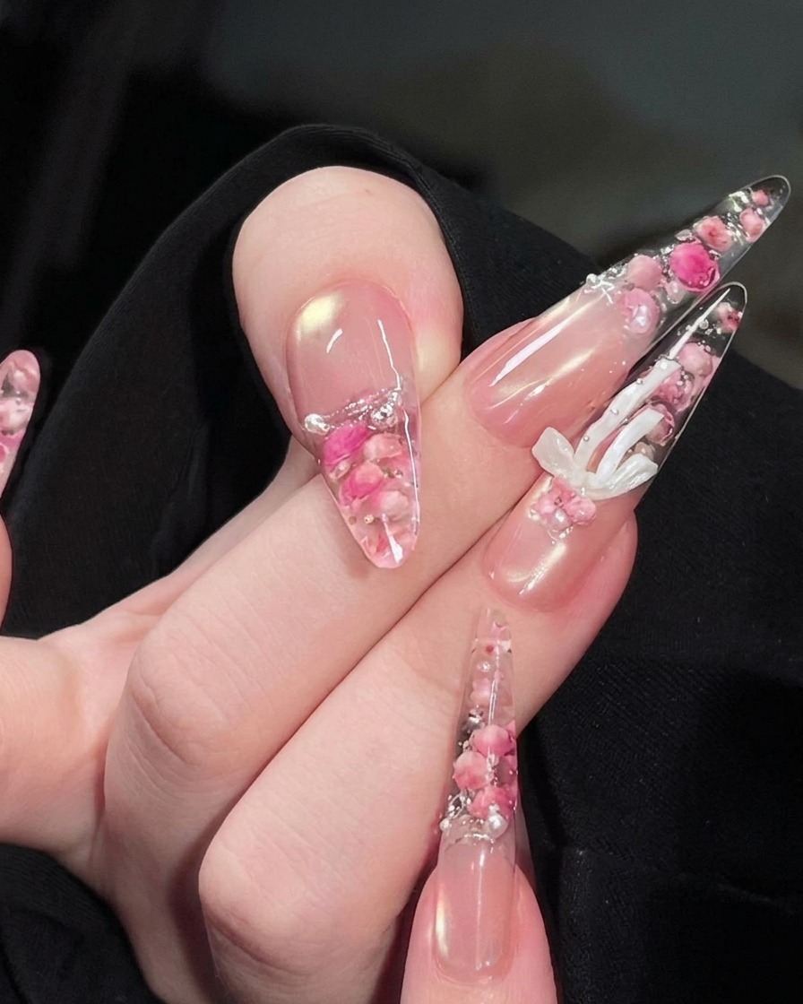 A hand positioned under a UV nail lamp, with the encapsulated rose and pearl design visible on the nails.
