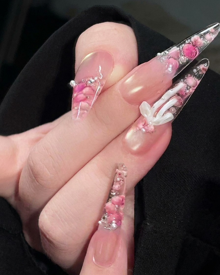 A brush applying a clear, glossy top coat to the surface of the finished rose nail design.