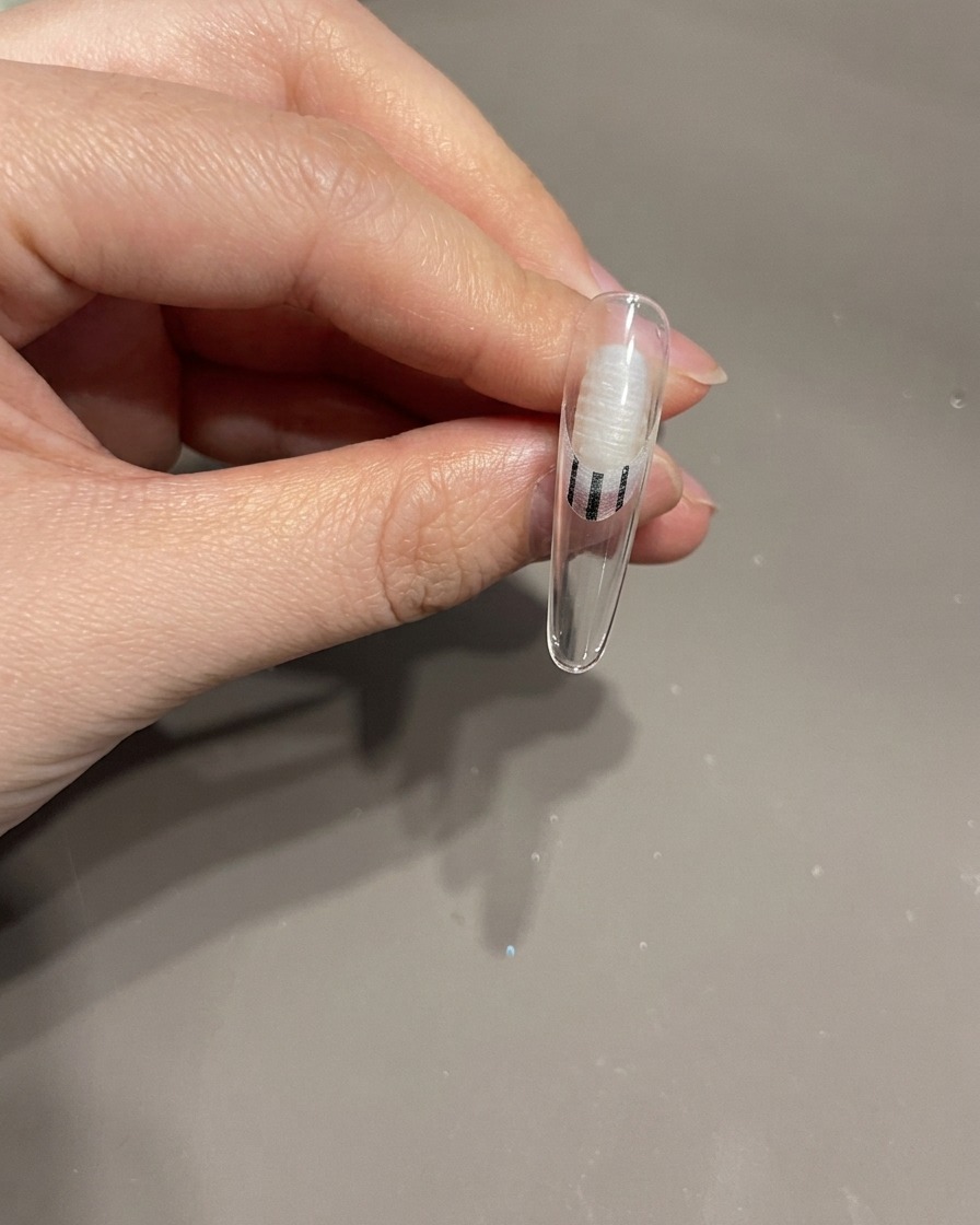 A close-up of a hand placing a fingernail with a 3D bow under a UV nail lamp for curing.