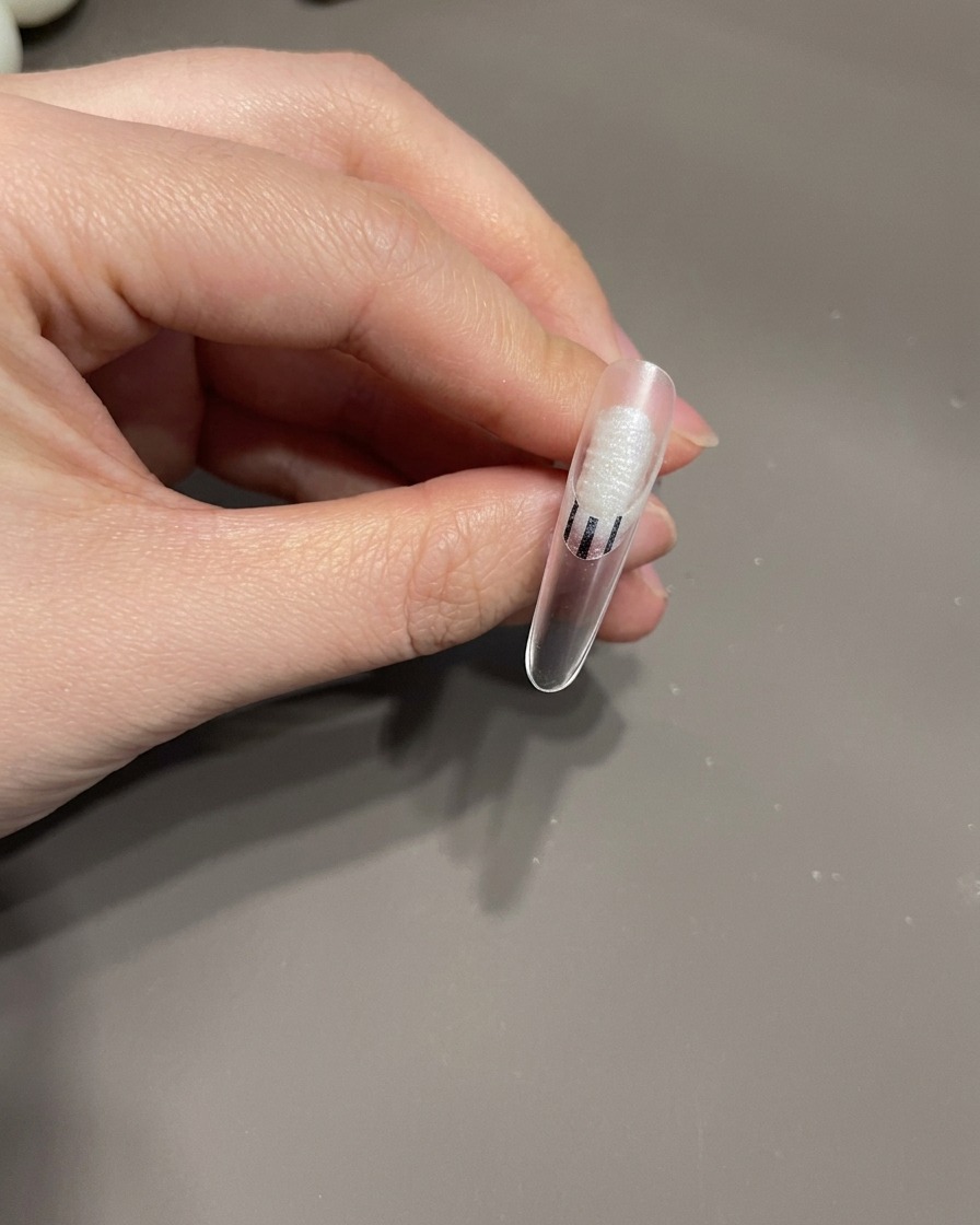 A detail brush drawing thin white lines in a swirl pattern over a gel-coated fingernail.