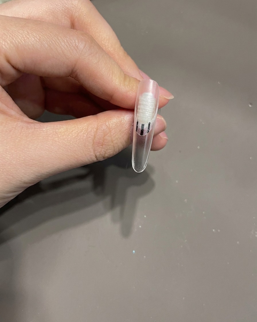 A nail brush applying a small drop of clear top coat onto a nail surface as glue for an embellishment.