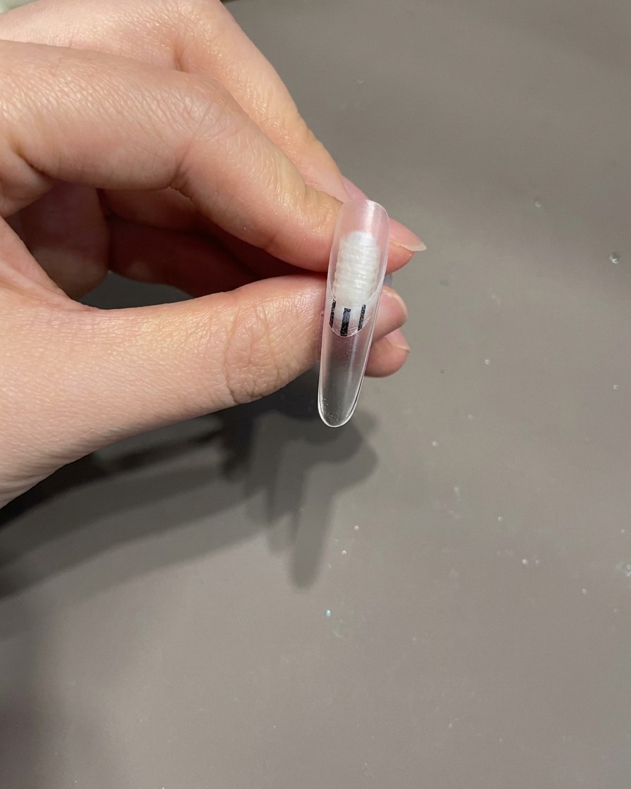 A finished fingernail with a 3D bow and swirling white lines inside a UV lamp for the final curing process.
