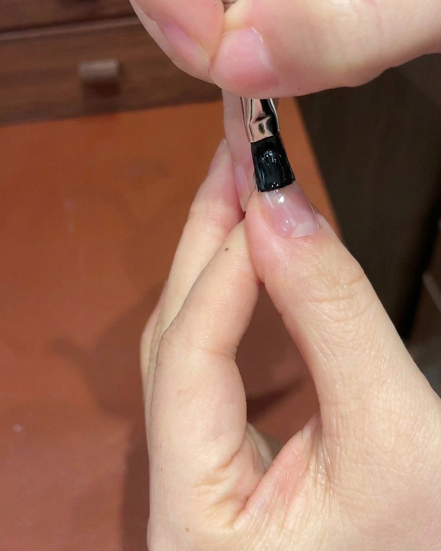 A close-up of a detail brush applying black gel to the free edge of a fingernail.