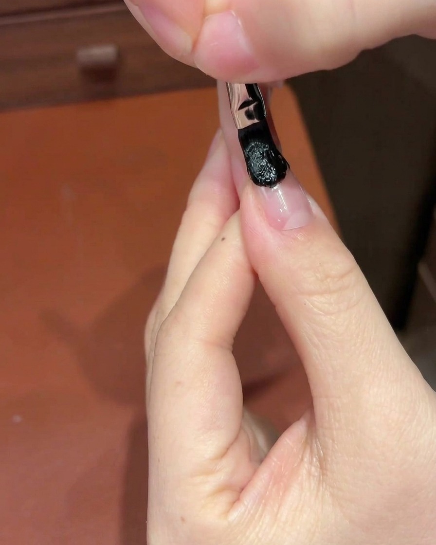 A white cosmetic sponge dabbing at a black gel section on a fingernail to create a gradient.