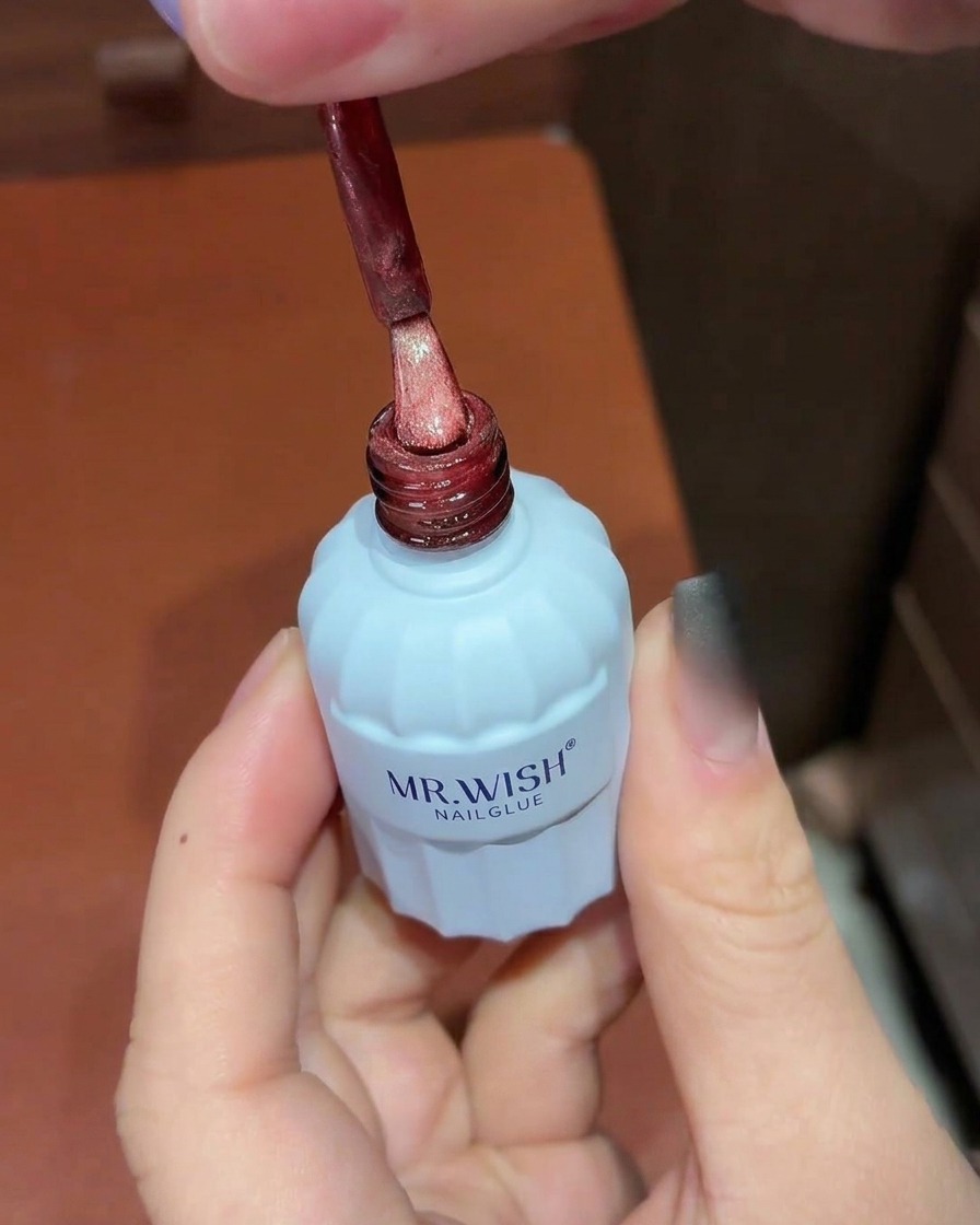 A brush applying red shimmering cat-eye gel polish over a black ombre nail.