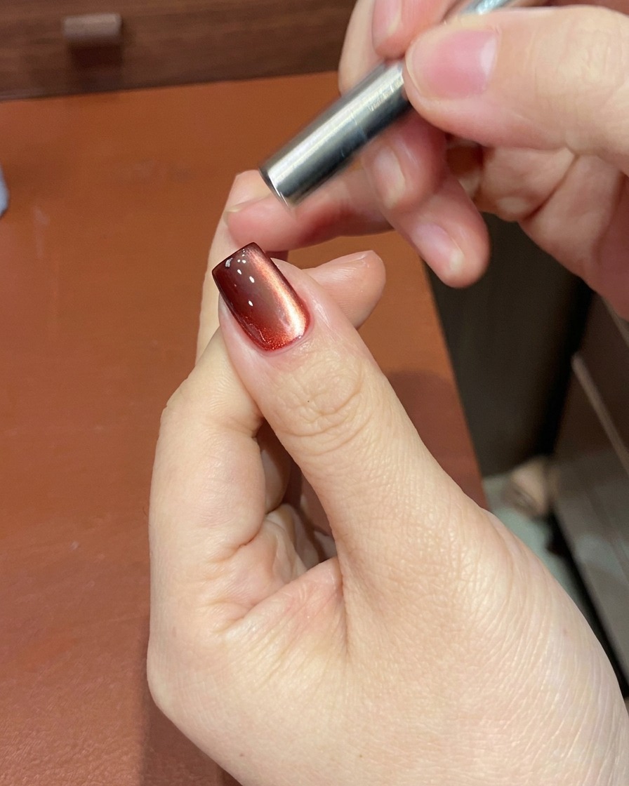 A magnetic tool positioned near a nail to manipulate the shimmer particles in the red gel polish.