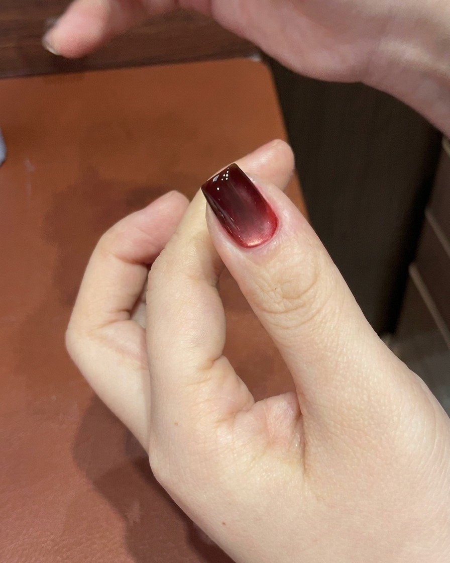 A red cat-eye gel nail being cured inside a UV/LED nail lamp, showing the set, glossy finish.