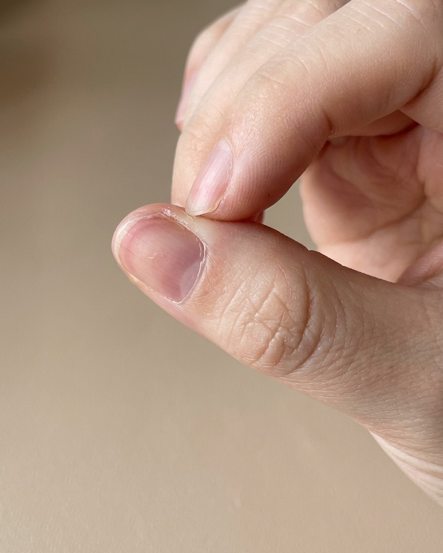A close-up of a cuticle oil pen being applied to the skin surrounding a freshly manicured nail.