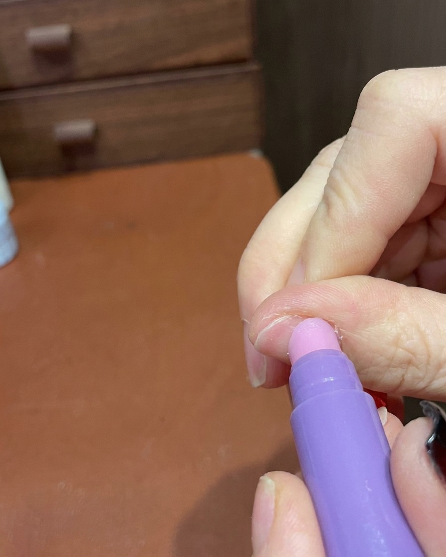 A close-up of a cuticle care pen being used to gently smooth the surface and edges of a finished manicure.