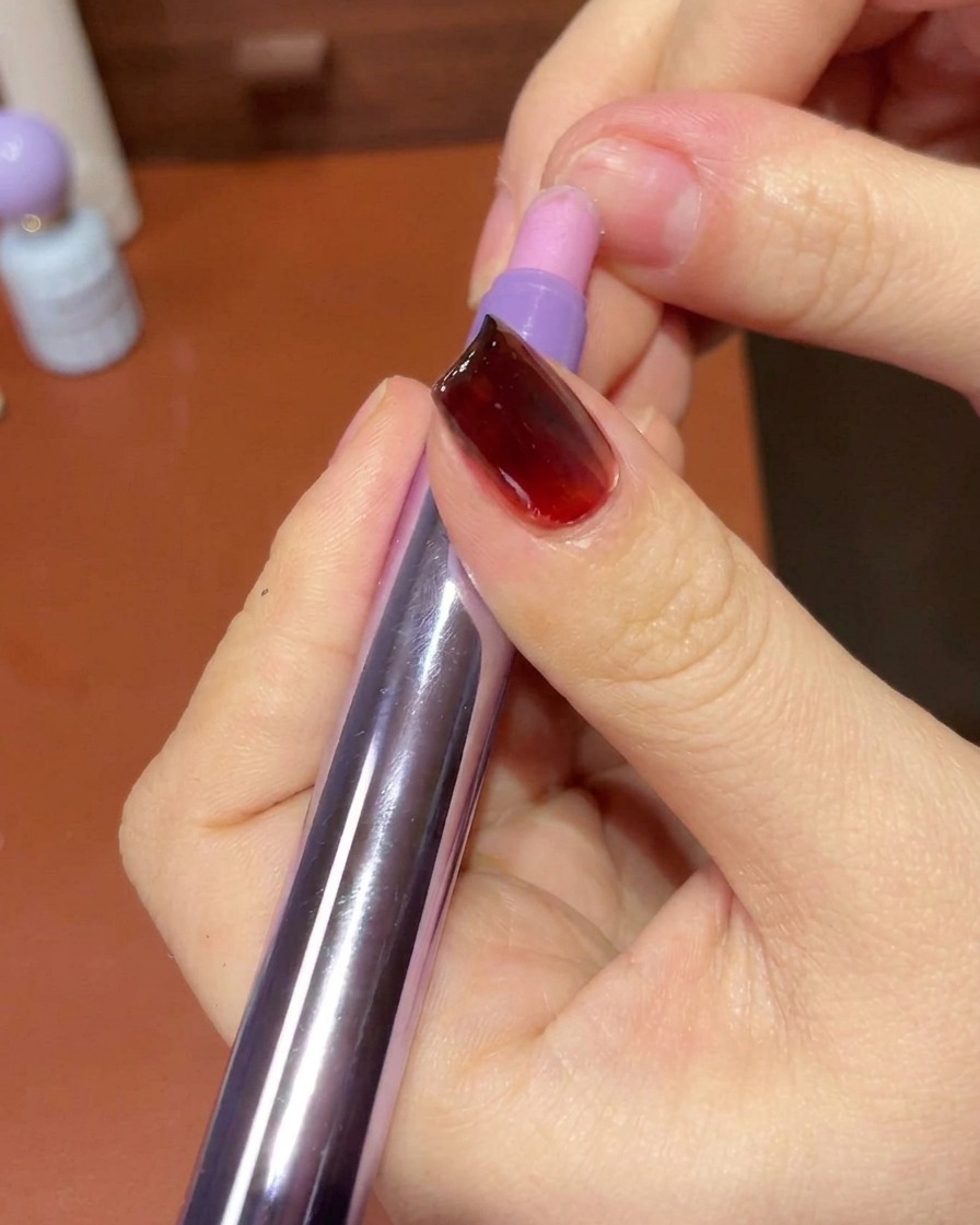 A hand using a lint-free wipe to clean the skin and edges around a finished gel-manicured nail.